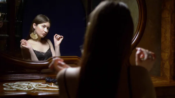 Piękna dziewczyna zakłada kolczyki, siedzi przed lustrem o zmierzchu. — Zdjęcie stockowe