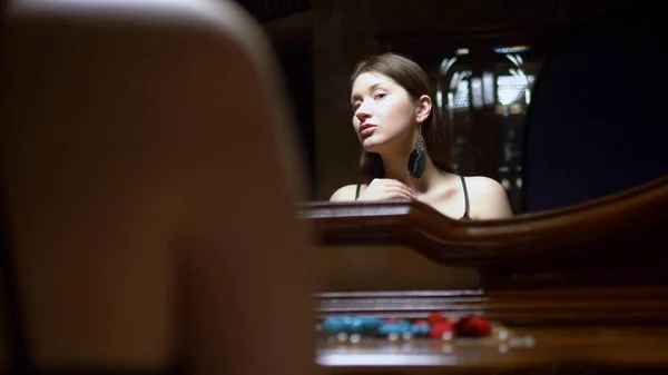 Gadis cantik memakai anting-anting, duduk di depan cermin saat senja . — Stok Foto