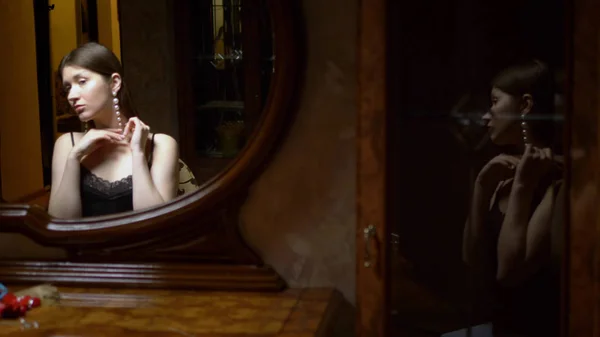 Beautiful  girl wearing necklace sitting in front of the mirror in the twilight. — Stock Photo, Image