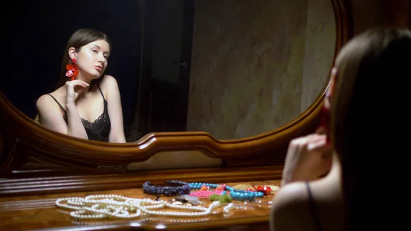 Красива дівчина одягає сережки, сидячи перед дзеркалом в сутінках . — стокове фото