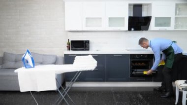 Önlük ve kravat takmış yakışıklı bir adam. Mutfağı temizler ve turta pişirir.