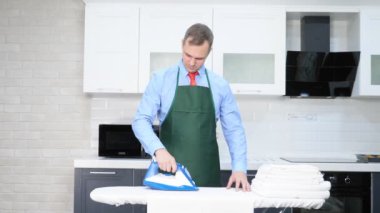 Kravatlı ve önlüklü yakışıklı bir adam çarşaf ütülüyor. temizlik kavramı