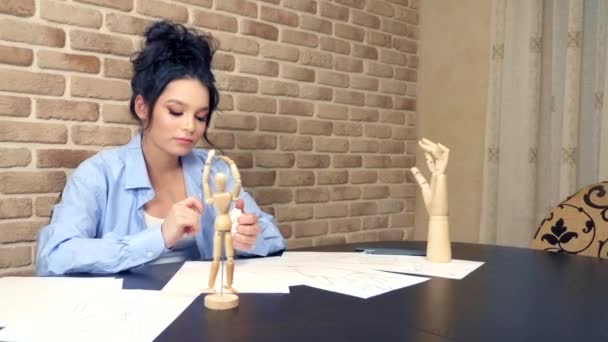 Mooi brunette meisje tekent een schets met een houten etalagepop — Stockvideo