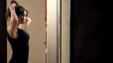 Kız, evinde aynanın önünde duran bir saç teli yapıyor.