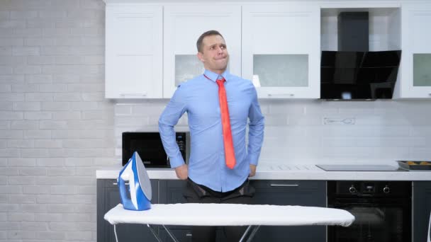 Κάθετη βολή. Όμορφος άντρας με γραβάτα να σιδερώνει παντελόνια. η κουζίνα του σπιτιού του — Αρχείο Βίντεο