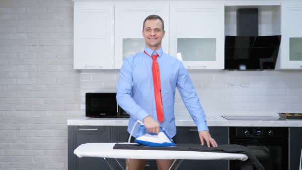Vertikalt skudd. Kjekken mann i slips som stryker bukser. kjøkkenet i huset hans – stockvideo