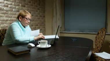 Evinde bilgisayarla belgelerle çalışan yaşlı bir kadın..