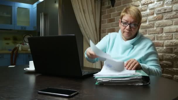 Ältere Frau, die zu Hause mit den Dokumenten am Laptop arbeitet. — Stockvideo