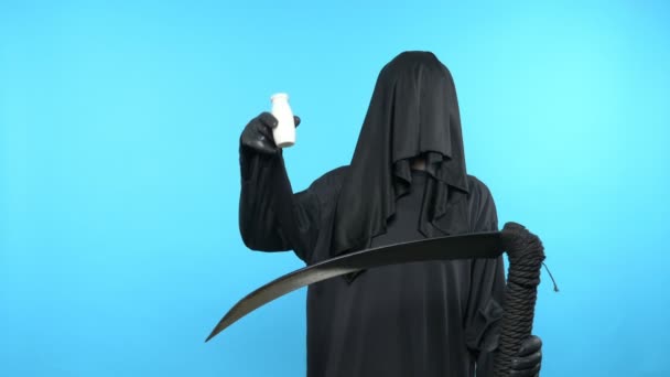 Человек в смертельном костюме с косой, показывает бутылку напитка. голубой фон — стоковое видео