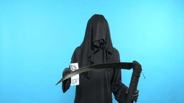 一个穿着死亡套装的男人拿着镰刀，展示避孕套。蓝色背景 — 图库视频影像