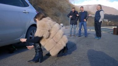 Erkekler yandan bakarken, bir kız arabanın tekerleğini değiştiriyor.