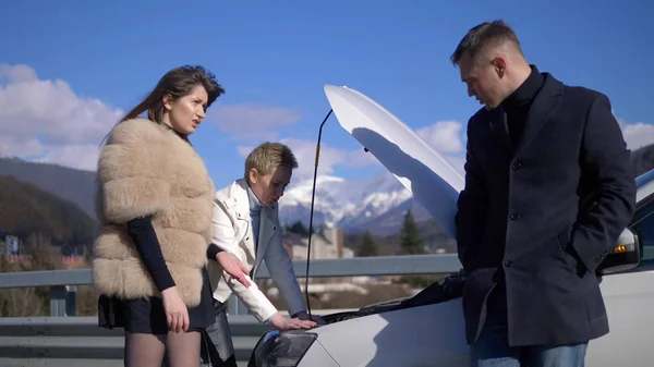 Two women repairing the car. a man stands nearby and looks at them — Stock Photo, Image