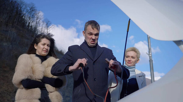 Две женщины ремонтируют машину. мужчина стоит рядом и смотрит на них
