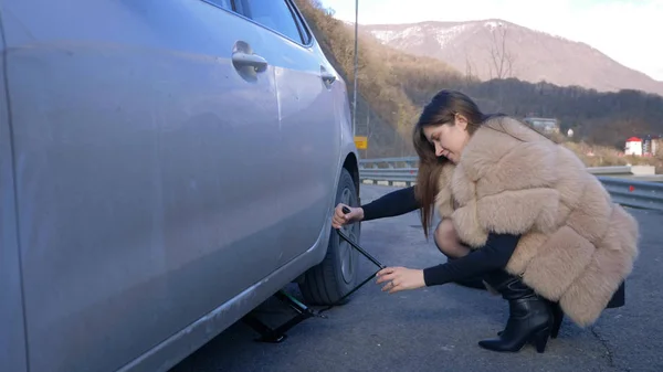 Красивая девушка меняет колесо автомобиля, припаркованного на обочине дороги — стоковое фото