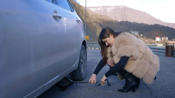 Beautiful girl changing the wheel of a car parked on the roadside — Stock Photo, Image