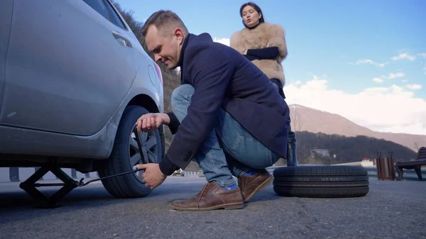 Un uomo cambia una ruota su una macchina, una ragazza è insoddisfatta lo rimprovera — Foto Stock