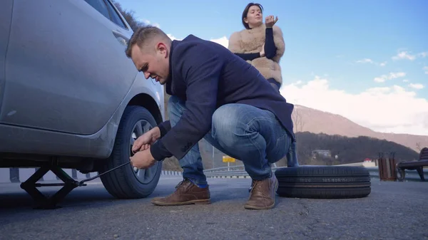 A man changes a wheel on a car, a girl is dissatisfied scolds him — Stok fotoğraf