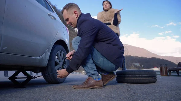 A man changes a wheel on a car, a girl is dissatisfied scolds him — Stok fotoğraf