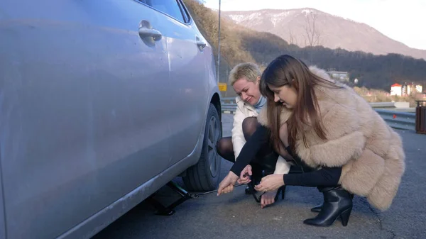 Two girls change a flat tire on the car on the side of the road. — Stock Photo, Image