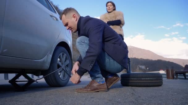 Un uomo cambia una ruota su una macchina, una ragazza è insoddisfatta lo rimprovera — Video Stock