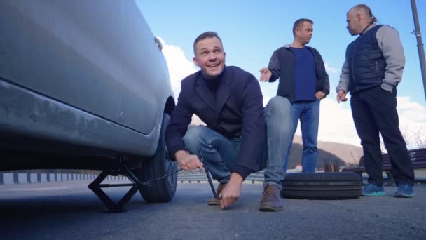 The man change the wheel, his friends watching him from the side — Stok video