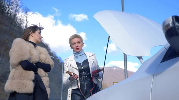 Two girls are charging the battery in a car standing on the side of the road — 스톡 사진