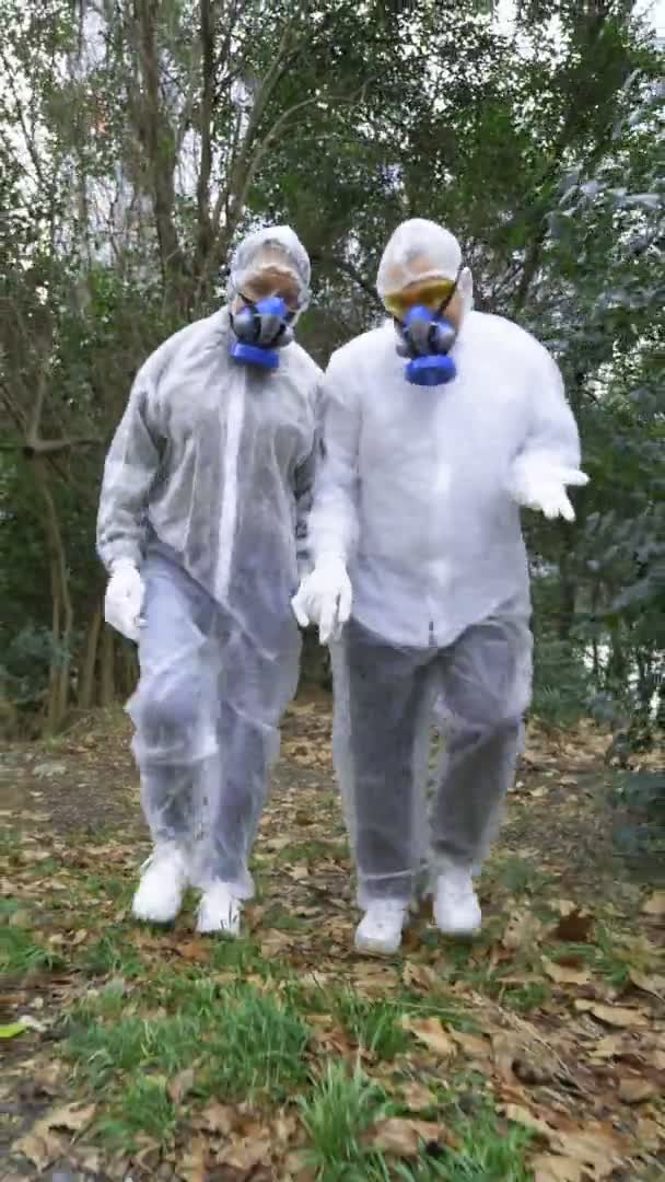 A man and a woman in protective suits and respirators, go to the Park — Stock Video