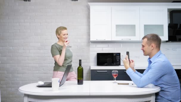 Ama de casa moderna y hombre de negocios descansando y bebiendo vino en la cocina — Vídeo de stock