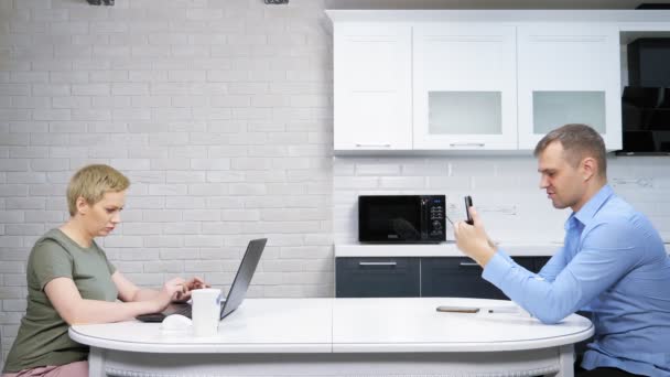 La femme au foyer moderne et l'homme d'affaires s'assoient à la cuisine, s'ignorant mutuellement — Video