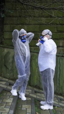 dikey, koruyucu giysiler ve solunum cihazları giymiş insanlar şehir parkında konuşuyor.