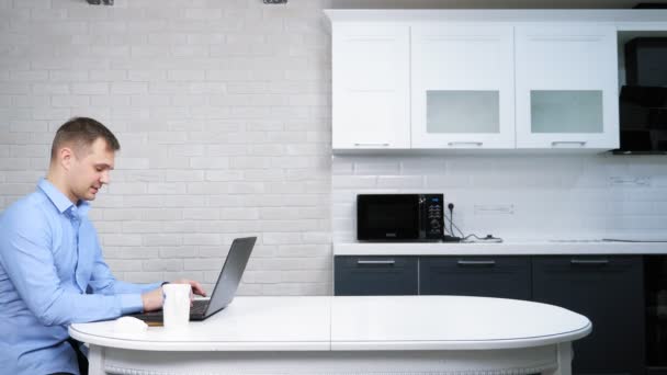 İş adamı mutfaktaki masada otururken dizüstü bilgisayarını kullanıyor. — Stok video