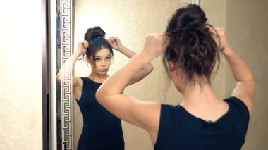 Kız, evinde aynanın önünde duran bir saç teli yapıyor.