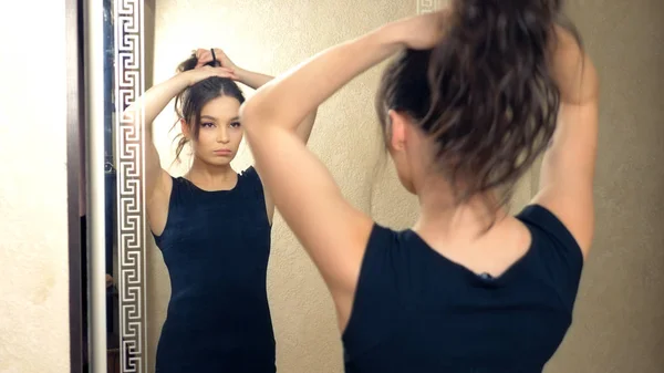 Девушка делает себе волосы, стоящие перед зеркалом дома — стоковое фото