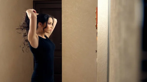 Девушка делает себе волосы, стоящие перед зеркалом дома — стоковое фото