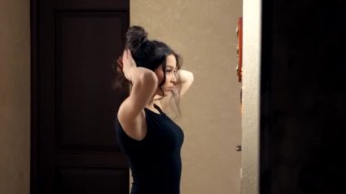 Kız, evinde aynanın önünde duran bir saç teli yapıyor.