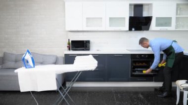 Önlük ve kravat takmış yakışıklı bir adam. Mutfağı temizler ve turta pişirir.