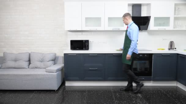 Um homem bonito de avental e gravata. limpa a cozinha no apartamento — Vídeo de Stock