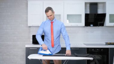 handsome man in tie ironing pants . the kitchen of his house