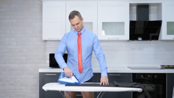 Bel homme en pantalon de repassage cravate. la cuisine de sa maison — Video