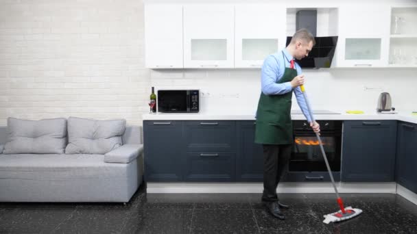 Hombre guapo en corbata y delantal trapea el suelo en la cocina — Vídeos de Stock
