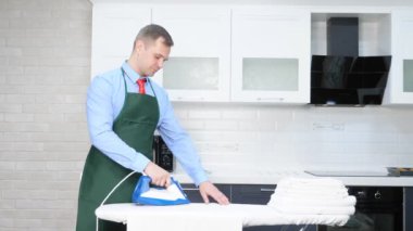 Kravatlı ve önlüklü yakışıklı bir adam çarşaf ütülüyor. temizlik kavramı