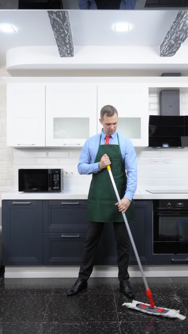 Vertikales Bild. schöner Mann in Krawatte und Schürze wischt den Boden in der Küche — Stockvideo