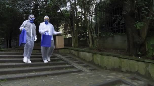 A man and a woman in protective suits and respirators, go to the Park — Stock Video