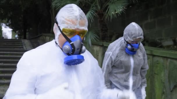 A man and a woman in protective suits and respirators, go to the Park — Stock Video