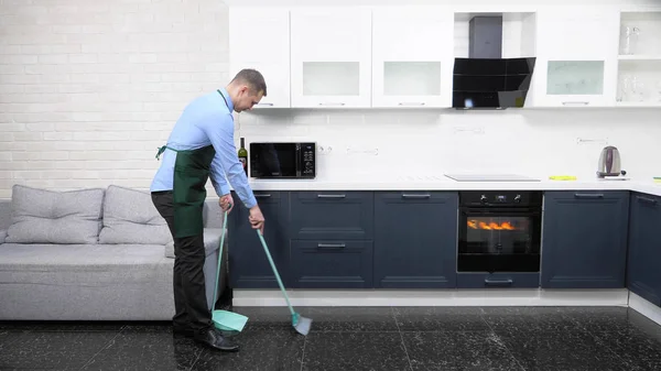 Hombre guapo en corbata y delantal barrer el piso de la cocina — Foto de Stock