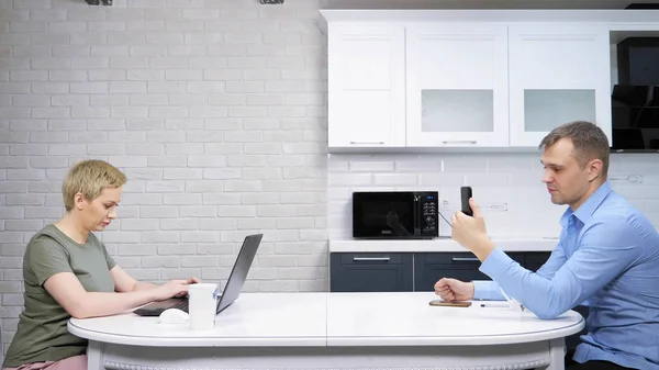 La femme au foyer moderne et l'homme d'affaires s'assoient à la cuisine, s'ignorant mutuellement — Photo