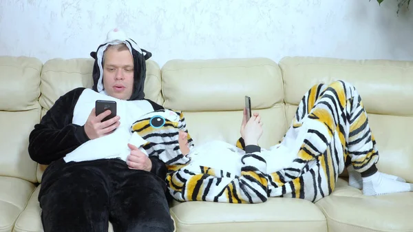 Чоловік і жінка в кігтях кіт і собака лежать на дивані і використовують смартфон — стокове фото