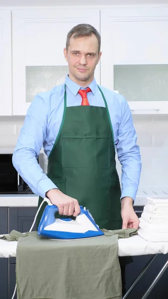 Vertical shot. handsome man in tie and apron stroking linen — Stock Photo, Image