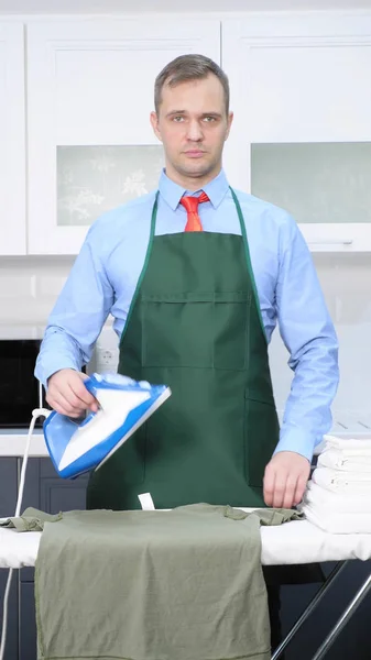 Vertical shot. handsome man in tie and apron stroking linen — Stock Photo, Image