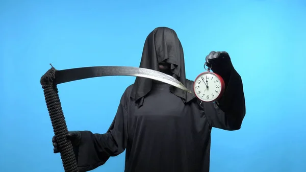 En man i dödsdräkt med lie visar en klocka. blå bakgrund — Stockfoto